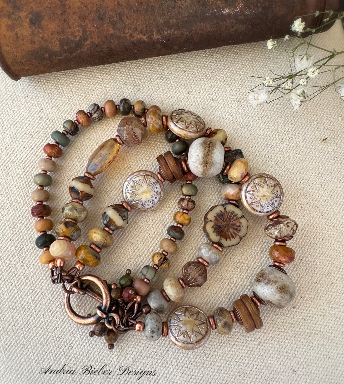 A multicolored beaded bracelet with a mix of jasper, ceramic, and copper metal components, displayed on a neutral background.